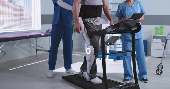 Man in exoskeleton walking on treadmill near rehabilitation therapists