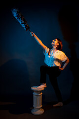 A girl stands on a miniature Greek column illuminated by multicolored light
