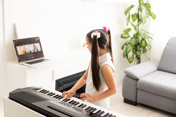 Homeschool little young kid girl learning piano from computer connecting to internet music online...