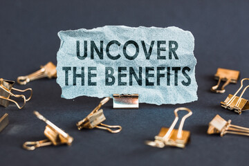 A scrap of blue paper with clips on a gray background with the text - UNCOVER THE BENEFITS.
