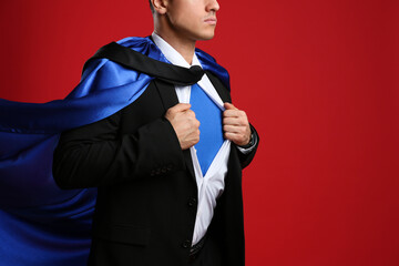Businessman in superhero cape taking suit off on red background, closeup