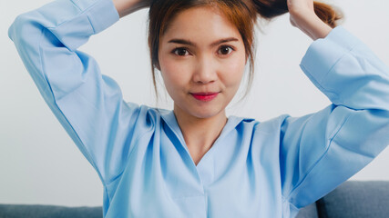 Young Asian woman doing long hair style looking in front mirror, Happy female make ponytail hairstyle to improve herself ready to working in bedroom at home. Lifestyle women at home concept. - obrazy, fototapety, plakaty