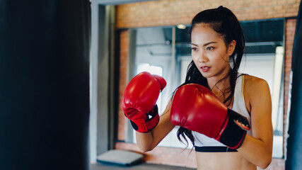 Young Asia lady kickboxing exercise workout punching bag tough female fighter practice boxing in gym fitness class. Sportswoman recreational activity, functional training, healthy lifestyle concept.