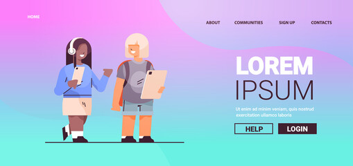 mix race schoolgirls using digital gadgets and listening to music in headphones