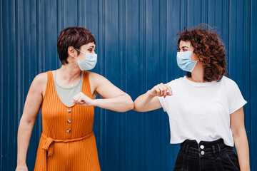 two caucasian women outdoors wearing face mask greeting with elbows. Pandemic during corona virus social distance concept. - obrazy, fototapety, plakaty