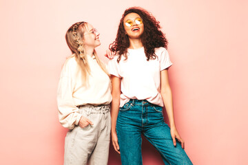 Two young beautiful smiling international hipster female in trendy summer clothes. Sexy carefree women posing near pink wall in studio. Positive models having fun. Concept of friendship