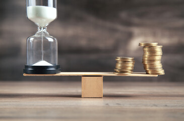 Hourglass and coins on the wooden balance.