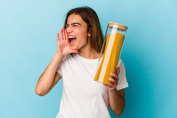 Young caucasian woman holding a pasta jar isolated on blue background shouting and holding palm near opened mouth.