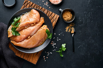 Raw chicken meat fillet marinated in teriyaki soy sauce, onions, garlic and pepper in black plate on a dark slate, stone or concrete background. Top view with copy space.