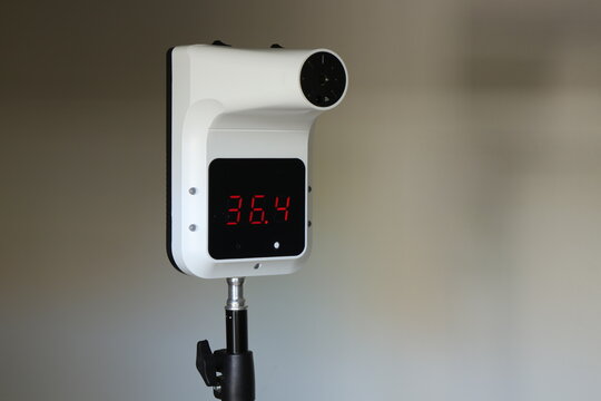 Red​ Digital​ numbers​ show​ the nomber 36.4​ On​ s​creen​ of​ a​ white​ thermometer​ on​ stand​ and​ blur​ed​ background.