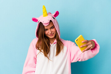 Young caucasian woman wearing a unicorn pajama holding a mobile phone isolated on blue background