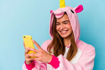 Young caucasian woman wearing a unicorn pajama holding a mobile phone isolated on blue background