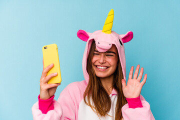 Young caucasian woman wearing a unicorn pajama holding a mobile phone isolated on blue background
