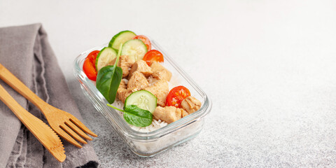 Chicken fillet with rice and vegetables in a glass container on the table. School, sports or business food concept