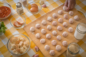 Woman's hand preparing fresh meatballs ready to be cooked, wooden cutting board and raw ingredients