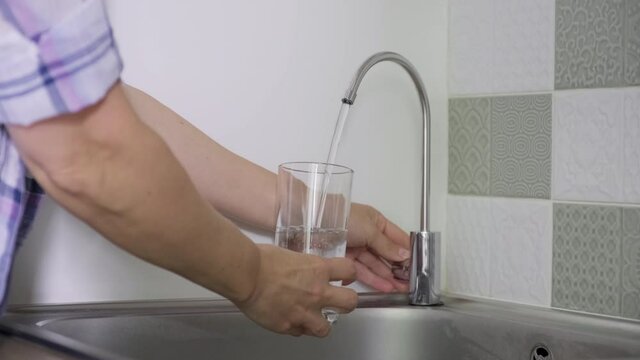 Close-up of hand with glass taking tap purified filtered water from special kitchen mixer