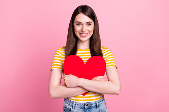 Photo of cute young teen lady hug paper heart wear orange t-shirt isolated on pastel pink color background