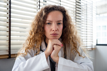 Serious female doctor carefully listening and keeping hands under chin while making medical...