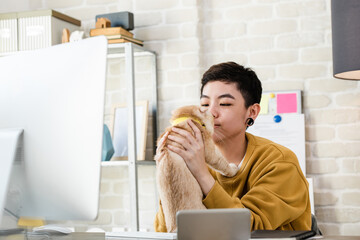 Young Asian tomboy woman in casual attire  holding her cat during working from home in living room