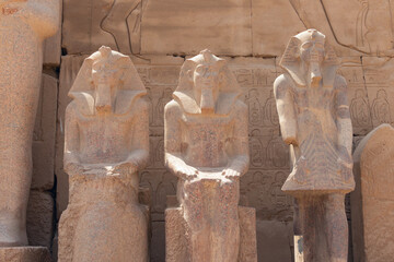 Granite statues of the ancient Egyptian pharaohs at the walls of the temple of Amun Ra in Luxor, in the background a wall with hieroglyphs