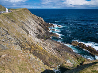 With the old Muckle Roe lighthouse above, steeply inclined, fractured rock strata on Sumburgh Head,...