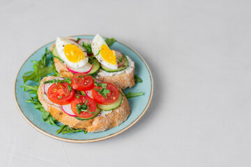 Delicious toasted sandwiches white bread with cream cheese, vegetables: cherry tomatoes, cucumbers, eggs, parsley. Healthy vegetarian breakfast idea. Served on craft paper, light background