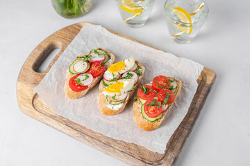 Healthy vegetarian breakfast idea. Toasted sandwiches white bread with cream cheese, vegetables: cherry tomatoes, cucumbers, eggs, parsley. Served on craft paper, light background