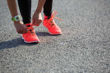 Fototapeta na wymiar Young fitness woman runner tying shoelace on road