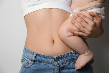 Fototapeta premium Mother with bare belly holding her baby on light grey background, closeup