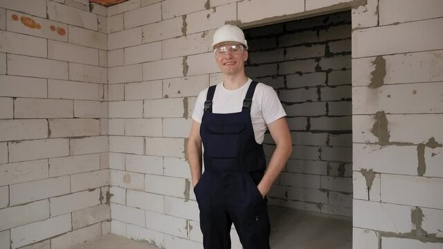 A male construction worker in overalls and a hard hat on a construction site.