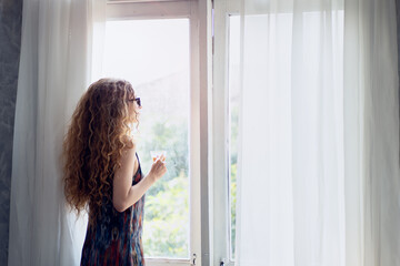 Young woman drinking coffee with opening the curtain in the morning
