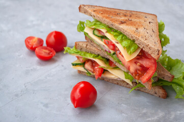 Delicious vegetarian sandwich with fresh lettuce leaves, tomatoes, cucumbers and cheese on a grey table background.