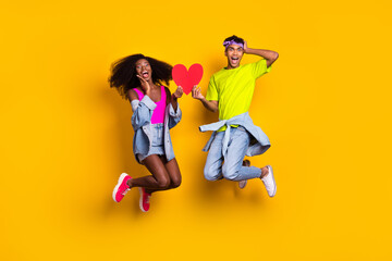 Fototapeta na wymiar Full length body size view of handsome beautiful trendy amazed couple jumping with red heart card isolated on bright yellow color background