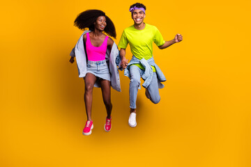 Fototapeta na wymiar Full length body size view of handsome beautiful trendy cheery couple jumping holding hands isolated on bright yellow color background