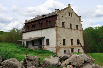Fototapeta na wymiar The building of an old abandoned mill of the 19th century on a green meadow near the stream
