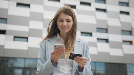 Fototapeta premium Smiling young woman customer holding credit card and smartphone. Happy female shopper using instant easy mobile payments making purchase in online store. E-banking app service. Online shopping.