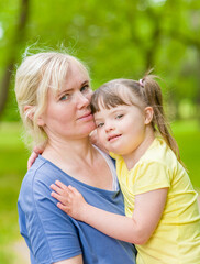 Smiling little girl with syndrom down hugs mother in a summer park