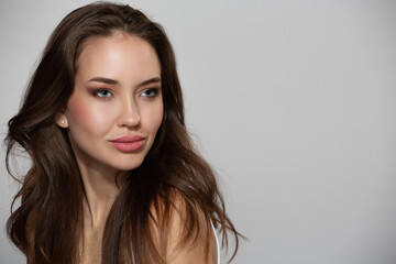 Obraz premium Portrait of beautiful young woman with natural skin make-up and brown hair on gray background