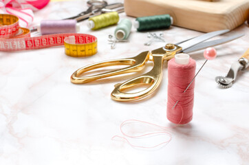Spool of pink thread,golden scissors,measuring tape,pins and other tools for sewing on the table