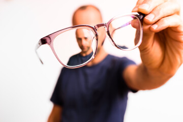 Mature man holds astigmatism glasses with plastic polymer lenses.