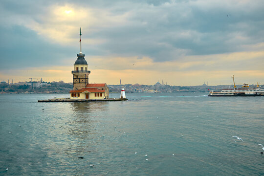 The maiden's tower (kiz kulesi) in stanbul, Turkey during overcast weather with sunshine reflection in bosporus sea.  Groups of seagulls flying on sea. stanbul Turkey 01.03.2021