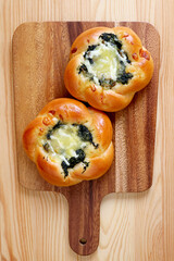 Pair of homemade spinach with cheese buns on a wooden breadboard