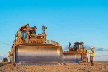 construction worker next to heavy machinery two yellow excavators at a construction site