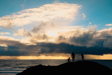 Fototapeta premium Epic image of storm brewing off the Australian coast over the beach in Mackay with silhoutte of a father and his sons on a hill in the foreground