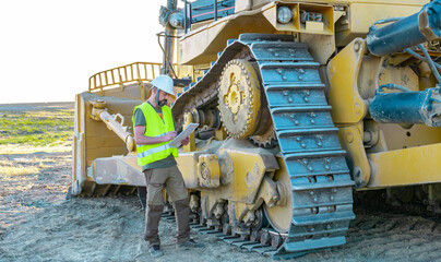 maintenance manager taking notes on an inspection of a heavy road making machine, bulldozer, large...