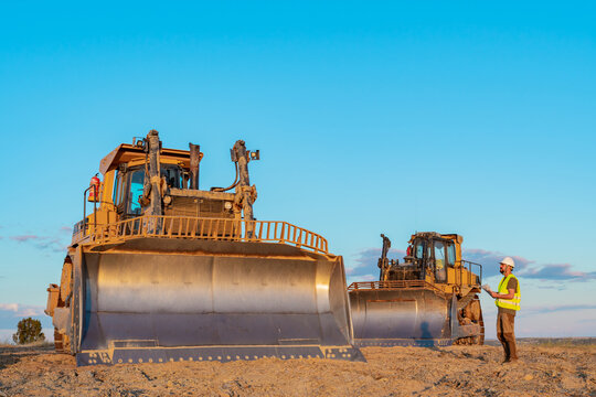 construction worker next to heavy machinery two yellow excavators at a construction site