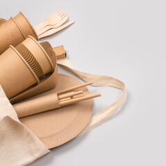 Square composition with eco-friendly tableware - kraft paper cups and containers in cotton bag on gray background with copy space for text. Street food take away paper packaging - cups, plates, straws