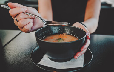 Woman hand eating chicken soup in black bowl sitting in cafe