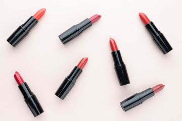Red lipsticks of different shades  in black tube package on beige background. Makeup and cosmetics...