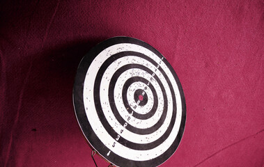 Already used and secondhand dart board standing on red carpet on ground and with its shadows.